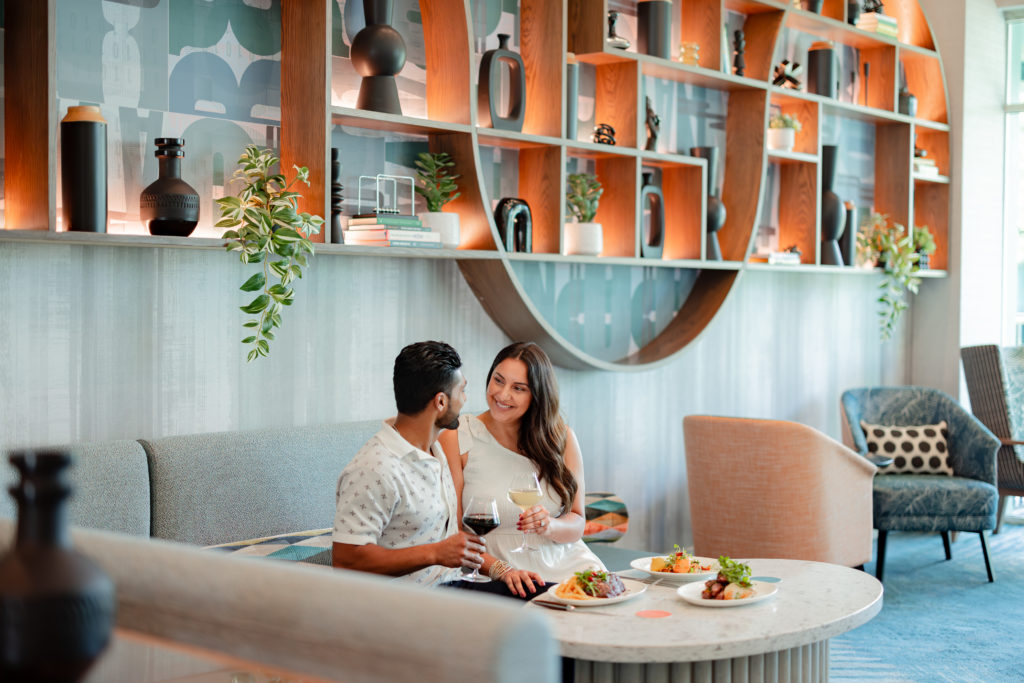 Couple looking at each other while holding wine glasses and dining at Émilie Bar + Lounge at Hotel Landy in Orlando, Florida