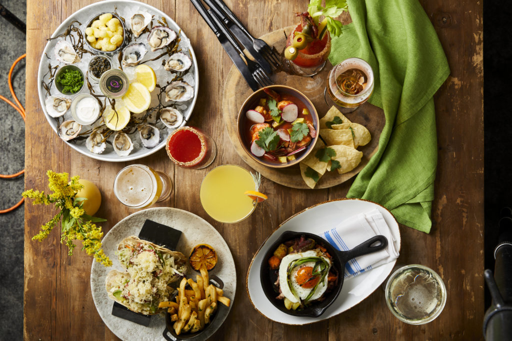 Flat lay of brunch dishes and cocktails at Salt Wood Kitchen & Oysterette at The Sanctuary Beach Resort in Monterey Bay